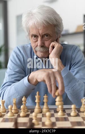 Selbstbewusster älterer Mann, der zu Hause Schach spielt, schaut auf die Kamera Stockfoto