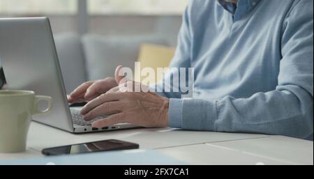Älterer Mann, der am Schreibtisch sitzt und sich mit seinem Laptop verbindet, die Hände aus der Nähe Stockfoto