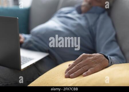 Älterer Mann, der auf der Couch einschläft, während er sich Videos ansieht Auf seinem Laptop Stockfoto