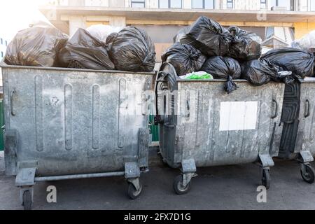 Reihen von vielen großen Metall überladenen Mülltonnen voller Schwarze Müllsäcke aus Plastik in der Nähe des Wohngebäudes in der Stadt Innenstadt oder Vorstadtbereich Stockfoto