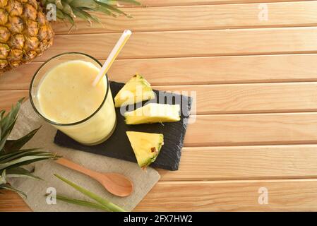 Zwei Gläser mit Ananassaft mit Milch und Ananasportionen auf einem Holztisch mit Ananas herum. Draufsicht. Stockfoto