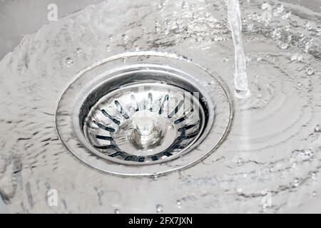 Wasser, das aus dem Wasserhahn in einem Waschbecken fließt und mit dem Filterstopfen in den Abfluss fließt. Stockfoto