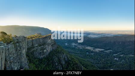 Ein Panoramablick von einem Grampians-Aussichtspunkt auf einen felsigen Felsvorsprung und in das Halls Gap Valley in Victoria mit brennenden Feuern in der Ferne. Stockfoto