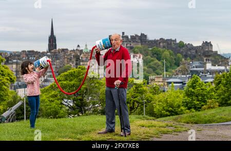 EMBARGO bis 10:00 Uhr Mai 26 2021. Calton Hill, Edinburgh, Schottland, Großbritannien, 26. Mai 2021. Der Programmstart des Edinburgh Science Festivals hat das Thema One World: Science Connects US, vertreten durch eine übergroße Blechdose mit Modellen in den diesjährigen Markenfarben Rot und Rosa. Im Bild: Die 8-jährige Winnie Maia verbindet sich mit Professor Peter Tasker durch riesige, mit einem Seil verbundene Zinnsuppendosen Stockfoto