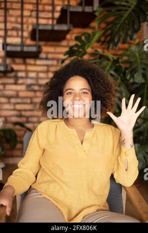 Videochat mit afroamerikanisch lächelnder Frau, die die Webcam begrüßt, horizontales Porträt. Fröhliche Frau hält Videoanruf, Begrüßung Online-Gesprächspartner, beteiligt Videokonferenz Stockfoto