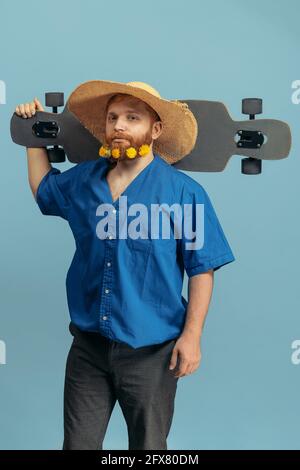 Junger Mann mit rotem Kopf und Bart in Strohhut, isoliert über blauem Untergrund stehend. Vergleich der Epochen Stockfoto