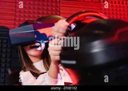 Staunend Teenager-Mädchen Rennen in vr Headset auf Auto-Simulator, verschwommen Vordergrund Stockfoto