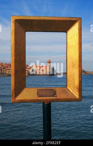 Ein ehemaliger leuchtturm der pharos in Gold gerahmt: Der Blick durch eine von 12 ‘Points 2 vue’ leeren Rahmenskulpturen, die der französische bildende Künstler Marc-André de Figueres um Collioure in Pyrénées-Orientales, Oskitanie, Frankreich, installiert hat, um den ikonischen Glockenturm der Église Notre-Dame-des-Anges (Kirche unserer Lieben Frau der Engel) aus verschiedenen Blickwinkeln zu sehen. Der 1959 geborene Künstler ist auch als Marc-André 2 Figueres und MA2F bekannt. Die Rahmen, jeweils 50 x 60 x 7 cm, sind aus Aluminium und vergoldeter Bronze gefertigt. Der Turm, der als mittelalterliches Leuchtfeuer erbaut wurde, wurde 1693 in einen campanile umgewandelt. Stockfoto