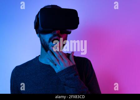 Der junge Mann, der eine VR-Brille mit offenem Mund trägt, staunte vor Ehrfurcht, isoliert auf einem farbenfrohen Hintergrund Stockfoto