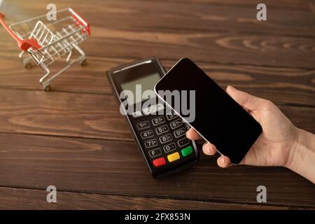 Weibliche Klientin hält Smartphone mit leerem Bildschirm und bezahlt für Bestellung mit moderner easy nfc-Technologie Stockfoto