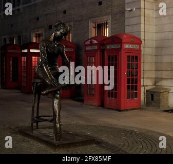 Skulptur der jungen Tänzerin von Enzo Plazzotta in Covent Garden bei Nacht mit roten Telefonzellen im Hintergrund. Stockfoto