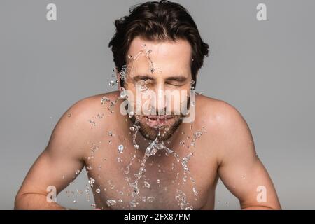 Bärtiger Mann mit geschlossenen Augen, der sich das Gesicht mit klarem Wasser wusch Isoliert auf Grau Stockfoto