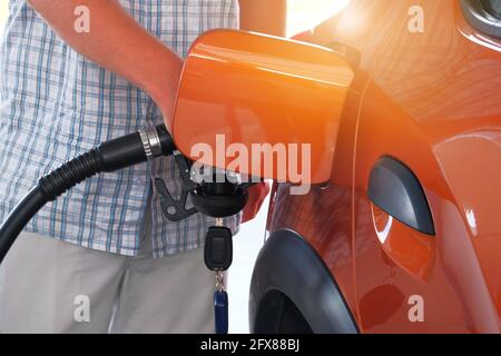 Pumpen von Benzin in einem orangefarbenen Auto an einer Tankstelle. Zum Tanken von Kraftstoff in der Tankstelle. Tankstellenpumpe. Sonnig. Stockfoto