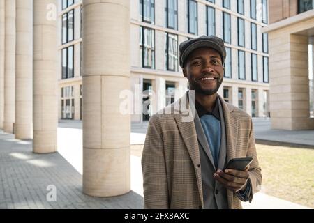 Porträt eines jungen afrikanischen Geschäftsmannes, der im Stehen die Kamera anlächelt In der Stadt Stockfoto