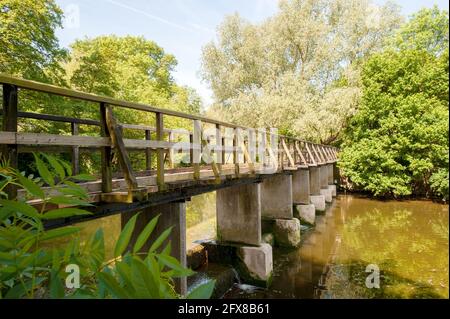 Holzfußbrücke auf Betonfüssen über stillem Wasser, Fluss und Wehr in ländlicher Lage in Essex Stockfoto