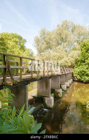 Holzfußbrücke auf Betonfüssen über stillem Wasser, Fluss und Wehr in ländlicher Lage in Essex Stockfoto