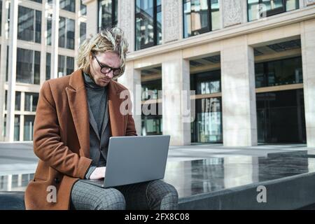 Junger Geschäftsmann in Brillen, der am Laptop tippt und online arbeitet Im Freien Stockfoto