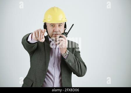 Porträt eines reifen Baumanagers oder Architekten in Hardhat-Zeigepointing Bei der Kamera während der Kommunikation über Walkie-Talkie Stockfoto