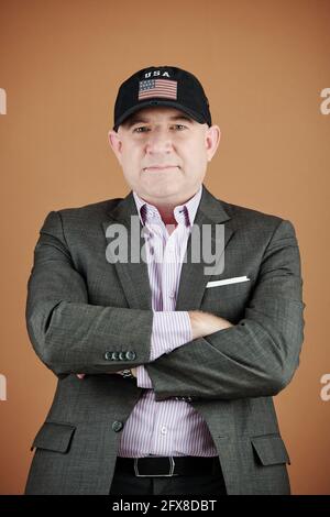 Porträt des Inhalts selbstbewussten amerikanischen Mann in Ballkappe und Formelle Jacke mit gekreuzten Armen vor isoliertem Hintergrund Stockfoto