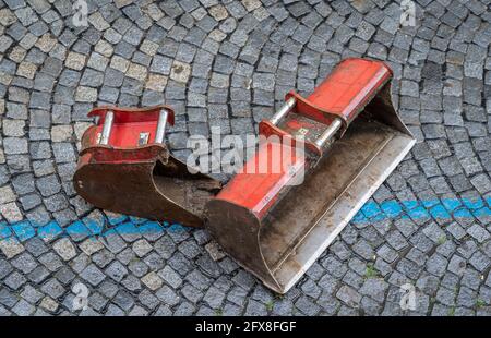 Bagger - Bagger - Eimer, klein und groß, ruht auf einer gepflasterten Straße Stockfoto