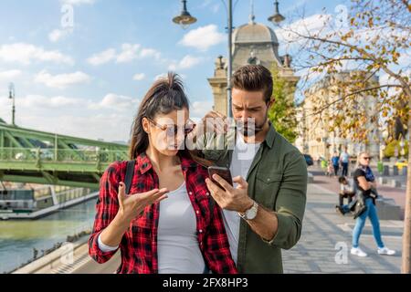 Ein junges Paar streitet über den Inhalt, der in einer europäischen Stadt auf dem Handy-Bildschirm zu sehen ist. Stockfoto