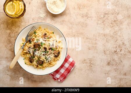 Italienische Pasta-Risoni, Pilze, Sauce, Parmesan, Thymian, Knoblauch, Olivenöl, in weißer Platte auf Schiefer, Stein oder Beton Hintergrund. Draufsicht mit Stockfoto