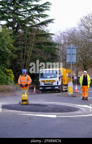 EPSOM, Großbritannien - CA. JANUAR 2019: Mann in gut sichtbarer Kleidung und einem Hut, der die Oberfläche mit einem Verdichter nivellierte Stockfoto