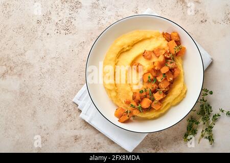 Polenta mit Butter, Kürbis, Knoblauch, Bohnenkraut und Parmesankäse in weißer Schale auf hellem Betongrund. Traditionelle, einfache italienische Küche, vegan Stockfoto