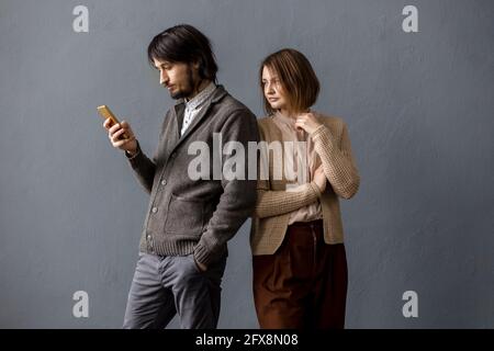 Der Mann schaut auf das Telefon und die Frau guckt von hinten. Grauer Hintergrund. Stockfoto