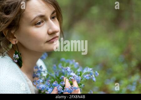 Mädchen hält einen kleinen Strauß von Vergissmeinnicht in ihren Händen und sieht allein zur Seite Stockfoto