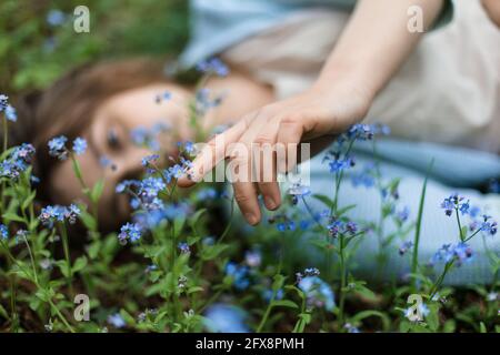 Mädchen liegt auf einer Wiese in Blumen von Vergissmeinnicht und läuft ihre Hand über sie. Stockfoto