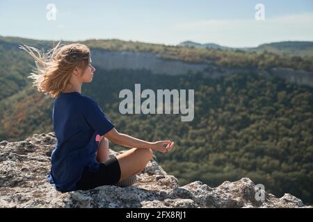 Die junge Frau sitzt auf einem Felsen, blickt auf die Landschaft und genießt die Aussicht und die frische Luft. Reisekonzept Stockfoto