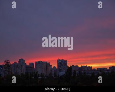 Erstaunlicher violetter, violetter, roter und gelber Sonnenuntergang über der Stadt Kiew (Kiew) mit Gebäuden, einem Beobachtungsrad und einer Kuppelkirche am Horizont. Industrie. Stockfoto
