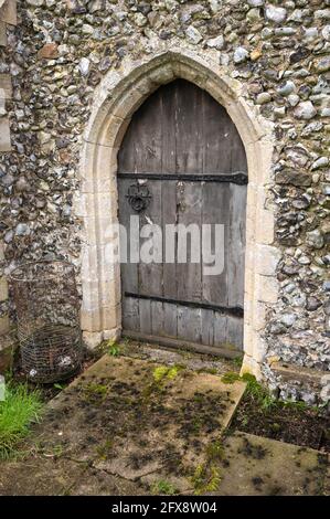 Eine alte Eiche gewölbte Tür mit langen geschraubten Scharnieren in Eine Steinmauer an einer Kirche im mittleren Norfolk-England Stockfoto