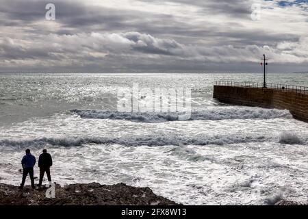 PORTHLEVEN, CORNWALL, UK - MAI 11 : stürmisches Wetter an der Hafenmauer in Porthleven, Cornwall am 11. Mai 2021. Zwei nicht identifizierte Personen Stockfoto