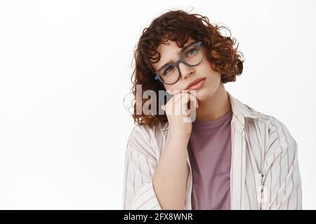 Porträt einer gelangweilten lockigen Schülerin in einer Brille, die sich an der Hand lehnt und mit Ansinnen schaut, gelangweilt und widerwillig starren, etwas langweilig hört Stockfoto