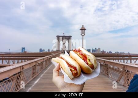 Halten von zwei Hot Dogs in NYC auf der Brooklyn Bridge . Stockfoto