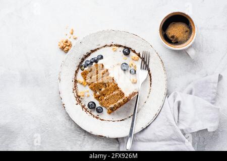 Ein Stück Karottenkuchen mit Walnüssen und Frischkäse-Zuckerguss, serviert mit frischen Blaubeeren auf einem Teller mit einer Tasse Kaffee, Draufsicht Stockfoto