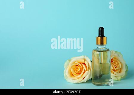 Flasche mit ätherischem Rosenöl und Rosen auf blauem Hintergrund Stockfoto