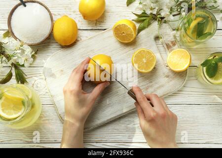 Weibliche Hände schneiden Zitrone für die Herstellung von Limonade auf weißem Holz Hintergrund Stockfoto