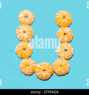 Kreatives Layout des Buchstabens U aus geschälten Mandarinen auf blauem Hintergrund. Flatlay. Stockfoto