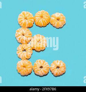 Kreatives Layout des Buchstabens E aus geschälten Mandarinen auf blauem Hintergrund. Flatlay. Stockfoto