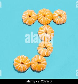 Kreatives Layout des Buchstabens J aus geschälten Mandarinen auf blauem Hintergrund. Flatlay. Stockfoto