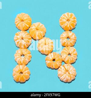 Kreatives Layout des Buchstabens N aus geschälten Mandarinen auf blauem Hintergrund. Flatlay. Stockfoto