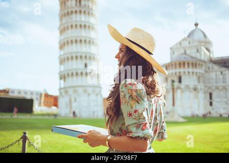 Glückliche junge Frau im Blumenkleid mit Pizza und Hut in der Nähe des Schiefen Turms in Pisa, Italien. Stockfoto