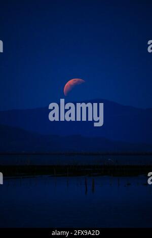 Taguig, National Capital Region, Philippinen. Mai 2021. Der Blutmond steigt hinter der Insel Talim auf, während die Mondfinsternis passiert. Blick von der C6 Road in Taguig City, Metro Manila. Quelle: George Buid/ZUMA Wire/Alamy Live News Stockfoto