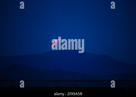 Taguig, National Capital Region, Philippinen. Mai 2021. Der Blutmond steigt hinter der Insel Talim auf, während die Mondfinsternis passiert. Blick von der C6 Road in Taguig City, Metro Manila. Quelle: George Buid/ZUMA Wire/Alamy Live News Stockfoto