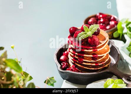 Gesundes Frühstück mit hartem Licht und Schatten. Hausgemachte klassische amerikanische Pfannkuchen mit Kirschsauce in einer gusseisernen Pfanne. Hausmannskost. Speicherplatz kopieren Stockfoto