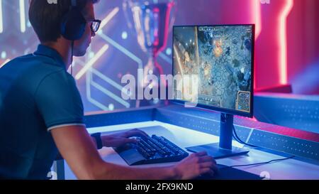 Professioneller eSports-Gamer spielt RPG MOBA Mock-Up Videospiel mit Super Action und Fun Special Effects auf seinem Personal Computer und spricht mit Teamkollegen Stockfoto