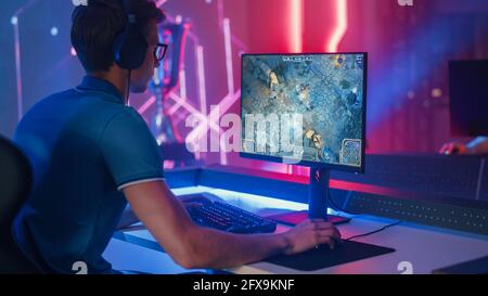 Professioneller eSports-Gamer spielt RPG MOBA Mock-Up Videospiel mit Super Action und Fun Special Effects auf seinem Personal Computer und spricht mit Teamkollegen Stockfoto